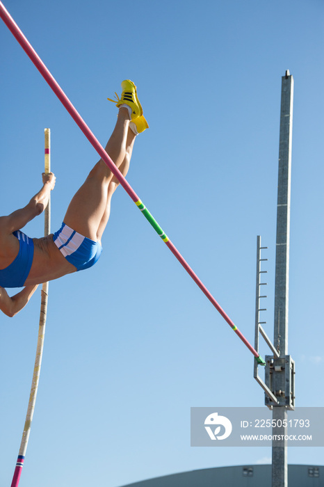 Female athlete pole vaulting under sunny bleu sky