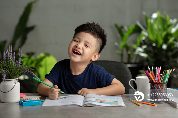 happy kid use color pencil drawing, having an idea on wooden table. Learning and education of kid