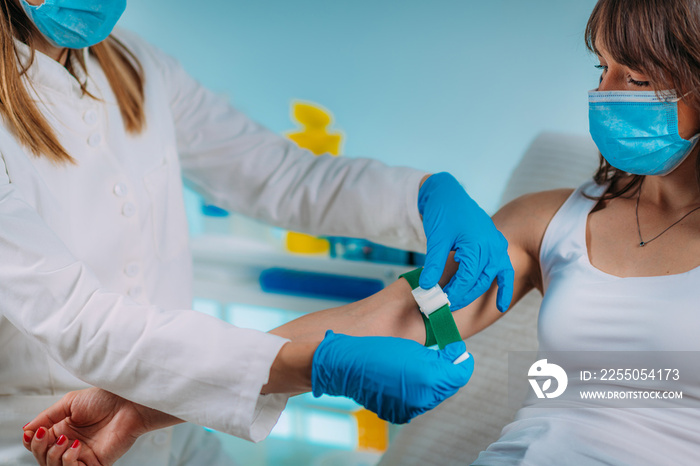 Preparation for phlebotomy procedure, female patient and medical nurse wearing protective masks