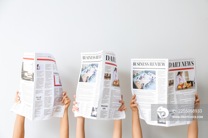 Female hands with newspapers on light background