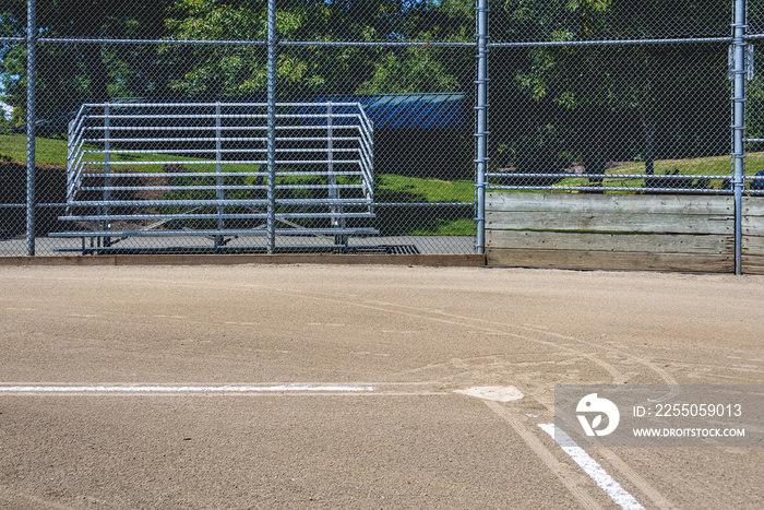 Close up of freshly chalked baseline leading to home plate, with backstop and bleachers, empty baseb