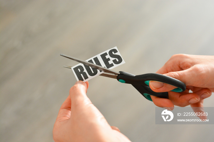 Woman hands cutting with scissors a printout reading  RULES