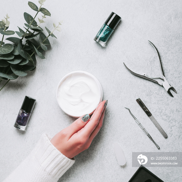 Woman hands, nail polish, manicure tools and hand cream on grey concrete table top flat lay. How to 