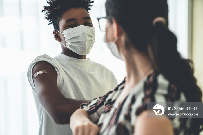 Smiling young people wearing face masks greeting merrily by bumping elbows at workplace . Teenage ma