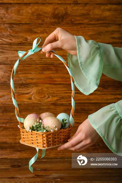 Woman holding wicker basket with painted Easter eggs on wooden background