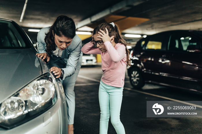 Frustrated and terrified mother and daughter looking at their scratched car.