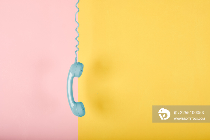 blue vintage telephone hanging on yellow and pink background