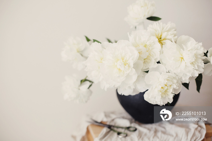 Happy Mothers day. Stylish peony bouquet in black clay vase on linen fabric with scissors on rustic background. White peonies rural still life. Hello spring wallpaper. Space text