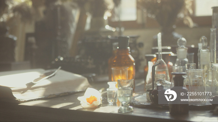 Close-up of a perfumer’s workplace. Vintage cinematic concept. Sunny day in the working workshop. Lots of ingredients, a book, glass flasks on the table. Depth of field