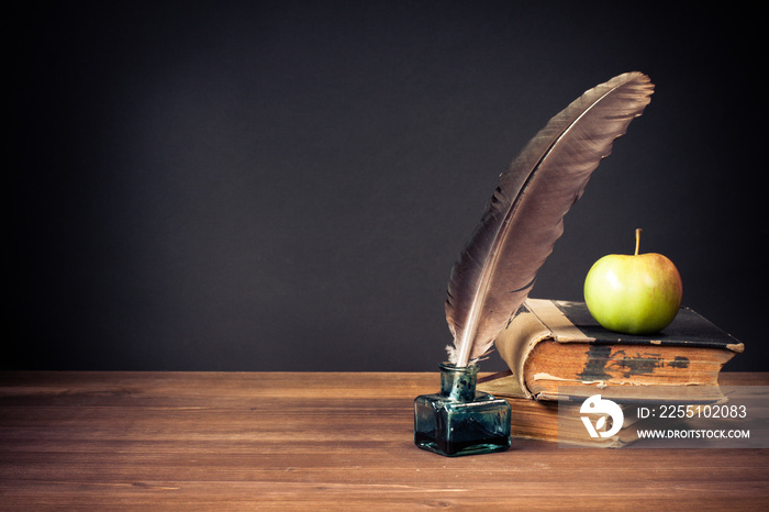 Quill pen, old books, apple on table for vintage background