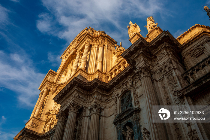 Detail of the monumental baroque facade of the cathedral of Murcia, Spain profusely decorated with sculptures and architectural details and creating a play of light and shadow at sunset