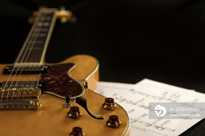 Vintage archtop guitar in natural maple close-up high angle view with music sheets on black background