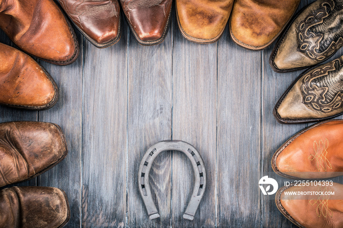 Wild West wooden background concept with retro leather cowboy boots and the horseshoe. Vintage style filtered photo