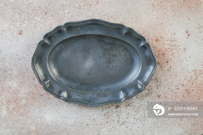 Antique pewter oval plate on concrete background.