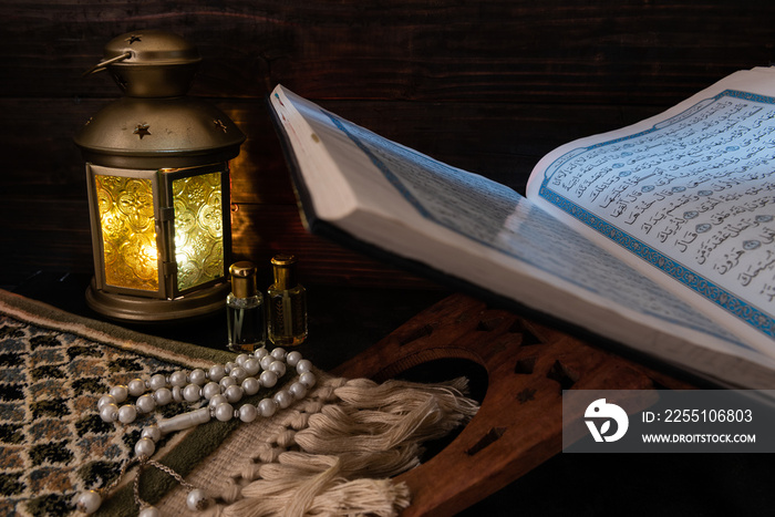 The Holy Quran placed with prayer rug, Ramadan lamp, praying mat and rosary beads. Islamic background.