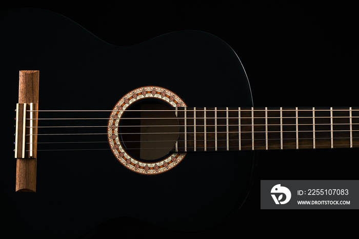 A black Six-string classical acoustic guitar isolated on black background.