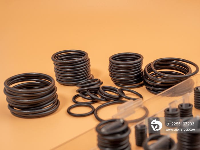 Hydraulic and pneumatic o-rings in black in different sizes on an orange background. Rubber gaskets for plumbing. copy space.