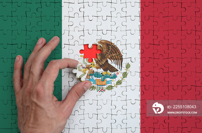 Mexico flag  is depicted on a puzzle, which the man’s hand completes to fold