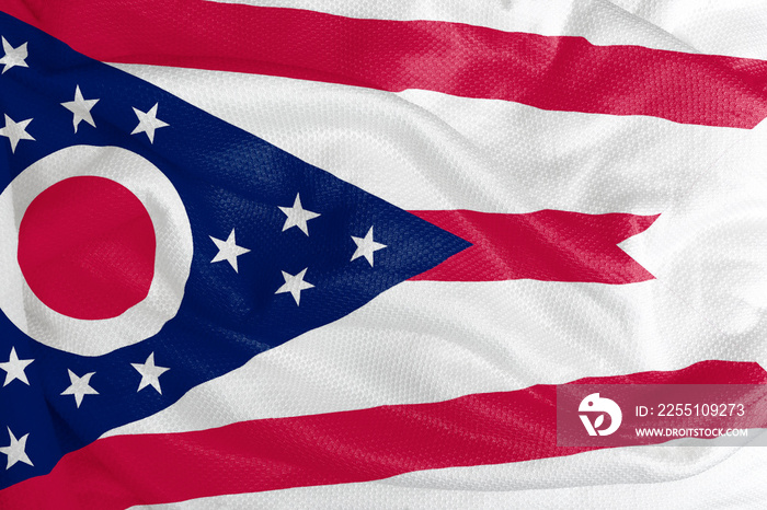 The Ohio flag is a large blue triangle, stripes and seventeen stars. The flag also has a white circle with a red center. The colors of the flag are blue, red and white.