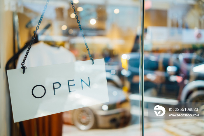 open sign welcoming customers hanging on glass door , in front of fashion clothing store in Bangkok