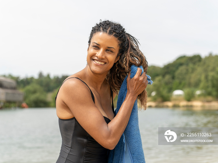 Portrait of smiling woman drying hair by lake