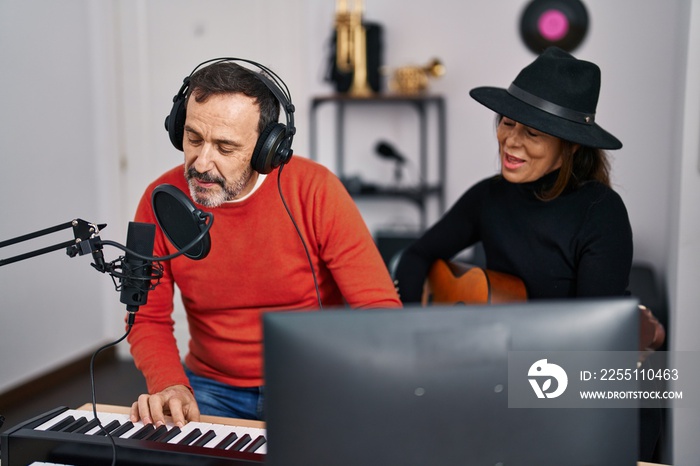 Middle age man and woman musicians playing guitar and keyboard piano singing song at music studio