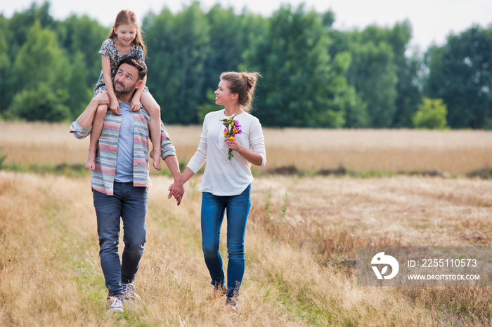 Young Caucasian family walking across field with young girl holding bouquet of flowers, concept organic ecologically friendly family