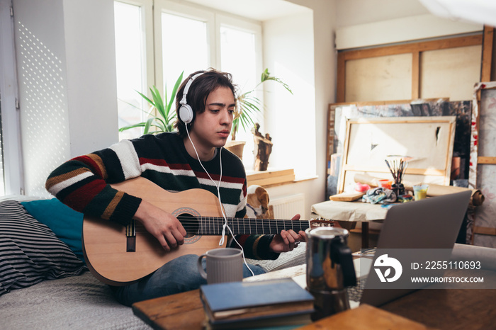 young man playing acoustic guitar in his room