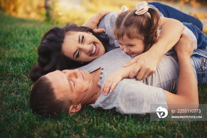 Happy pregnant family with little girl laying on grass and having fun in summer nature