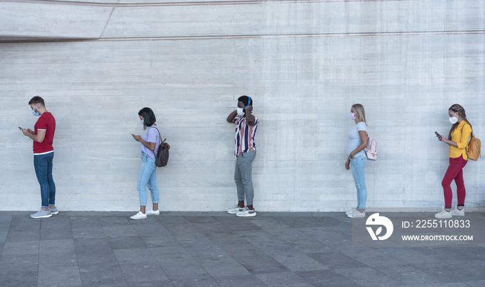 Group of young people waiting for going inside a shop market while keeping social distance in line during coronavirus time - Protective face mask and spread virus prevention - Main focus on black man