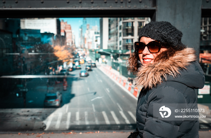 Beautiful curly brunette woman on the high line watching the street, while sightseeing New York City during winter season. Tourist in Highline park NYC