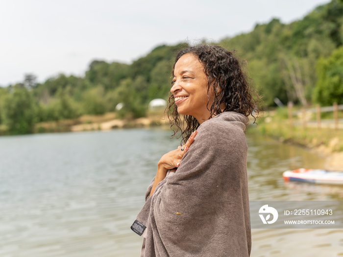 Smiling woman wrapped in towel standing by lake