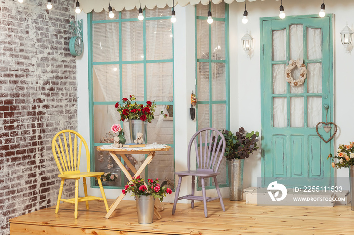 Garden table and chairs on the summer porch of the house. Summer terrace with retro light bulbs garlands. Beautiful porch with spring decorations in the photo Studio