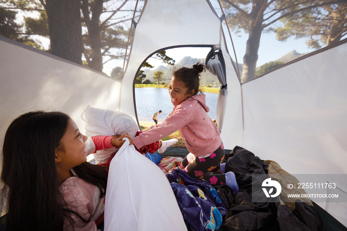 Little girls pillow fighting in tent during family camping holiday