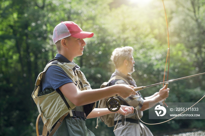 A father and his son fly fishing in summer on a beautiful trout river with clear water