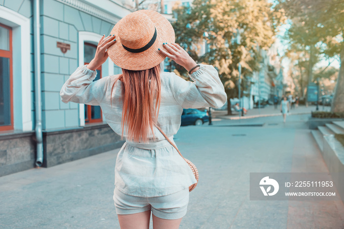 Female fashion concept. Outdoor portrait of young beautiful fashionable lady walking on the street. Model wearing stylish hat and clothes. Sunny day. Back view. Waist up. Copy space for text