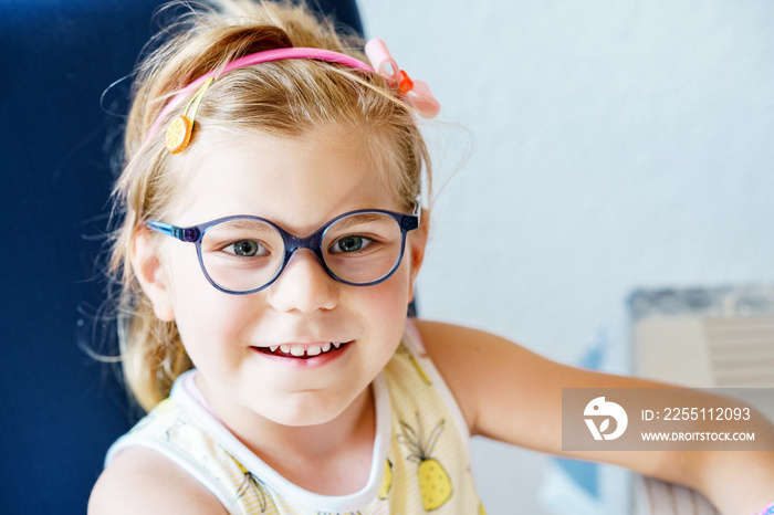 Portrait of a cute preschool girl with eye glasses indoors. Happy funny child wearing new blue glasses.