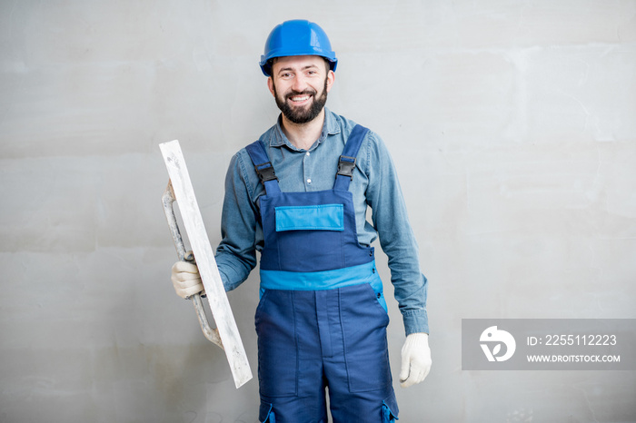 Portrait of a handsome builder in blue working uniform plastering the wall indoors