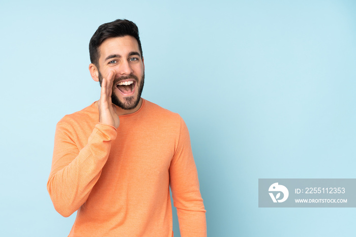 Caucasian handsome man shouting with mouth wide open over isolated blue background