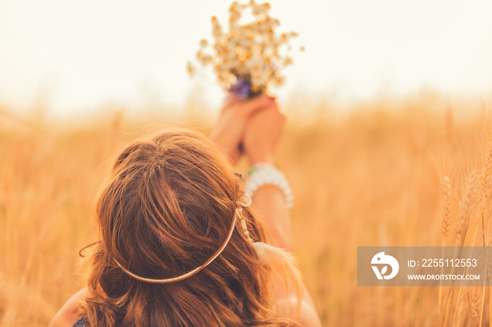 Girl holding flower bouquet in wheat field.