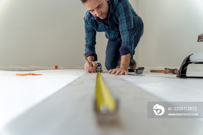 close up of man measuring the floor to install wooden decking in his house