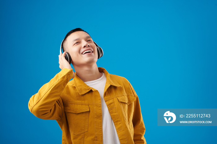 Happy young man singing to the music in his headphones, isolated on blue