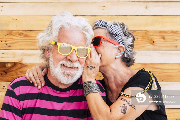 Youth people caucasian couple of cheerful alternative senior whispering secrets and enjoy the life togther - wood background and youthful retired lifestyle