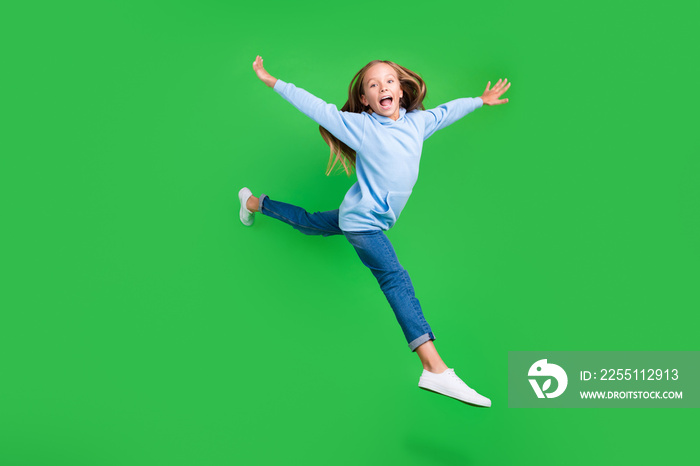 Full length photo of sporty adorable small girl jump spread hands have fun wear stylish blue sportswear isolated on green color background.