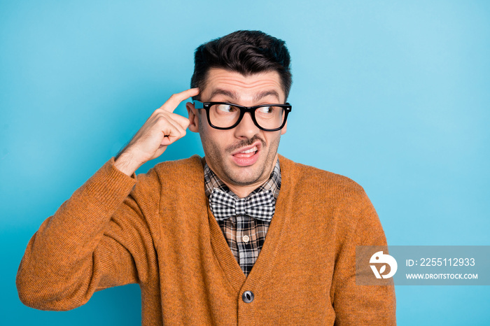 Photo of doubtful young brunette man point finger head look empty space isolated on pastel blue color background