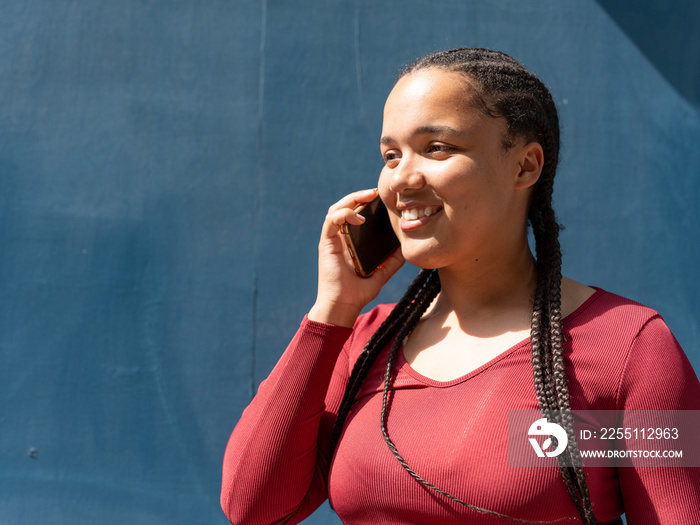 Portrait of young woman talking by phone against blue wall