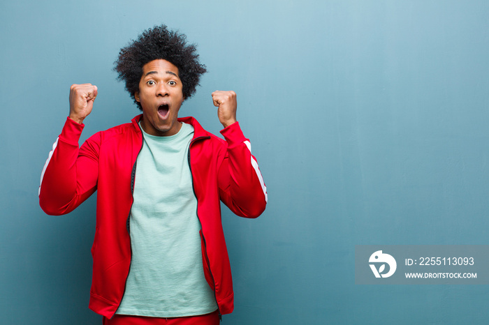 young black sports man celebrating an unbelievable success like a winner, looking excited and happy saying take that! against grunge wall