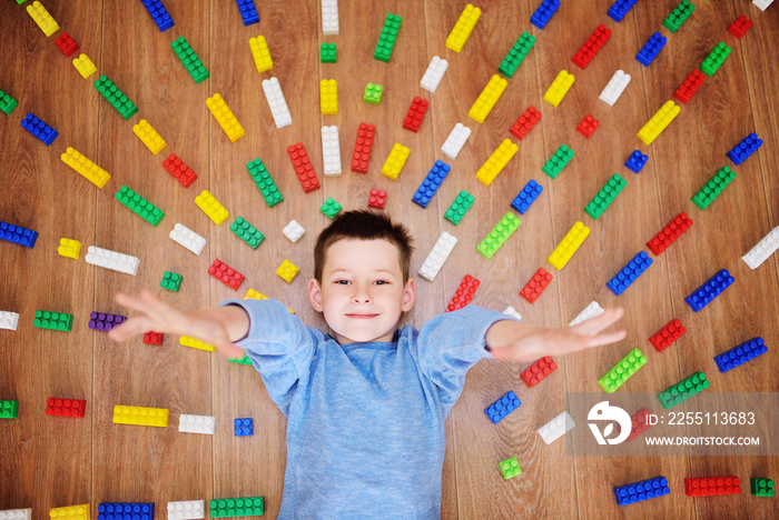 a small child boy is smiling against the background of colorful blocks of children’s construction set with rays on the floor. Concept of childhood, games.