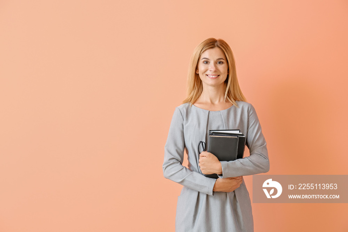 Beautiful female teacher with books on color background