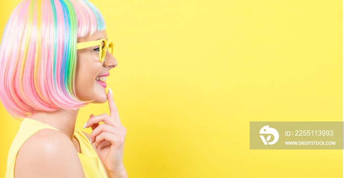 Young woman in a colorful wig with sunglasses on a yellow background